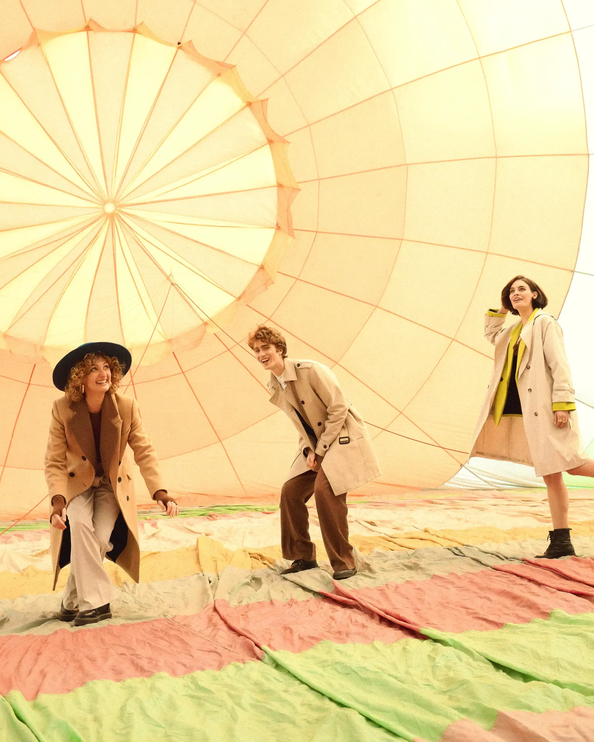 Three individuals, dressed in beige coats, joyfully interact inside a hot air balloon, illuminated by warm, diffused light.