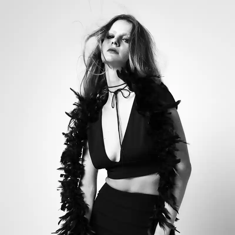 Black and white portrait of a woman in a provocative outfit, wearing a deep V-neck top and a feather boa, with a confident and rebellious expression by Juan Lamas Photographer.