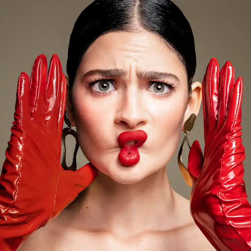 Close-up of a woman with red gloves making a playful face with puckered red lips by Juan Lamas Photographer.