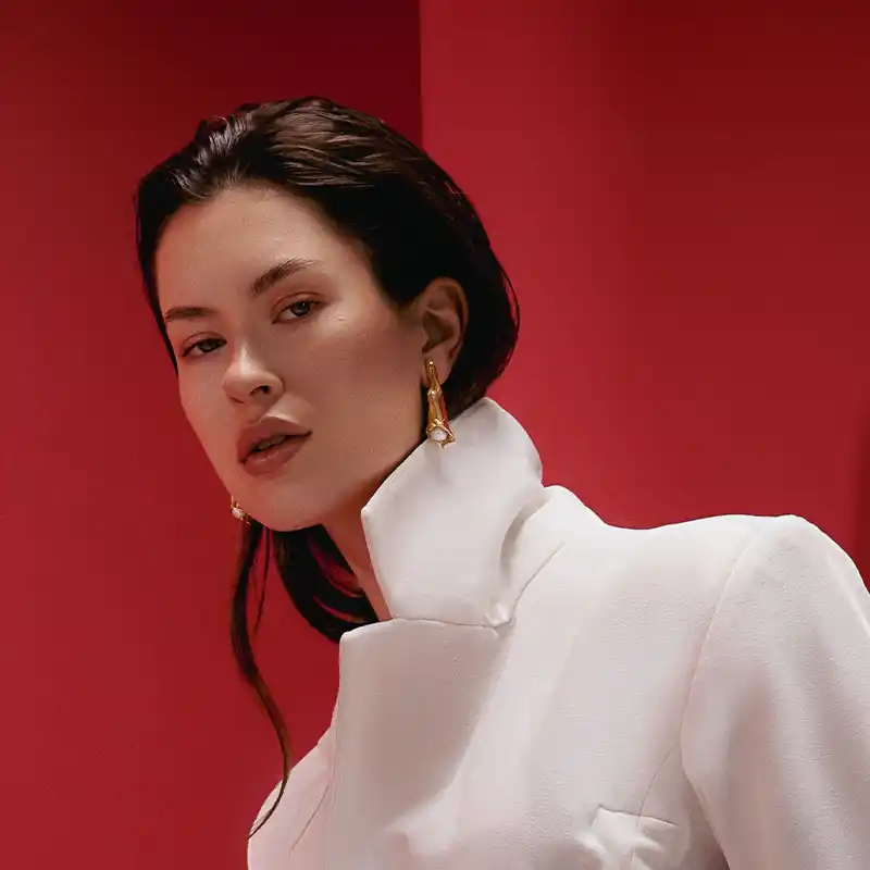 A sophisticated woman in a white suit jacket posing confidently against a vibrant red background by Juan Lamas Photographer.